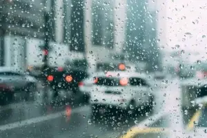 A blurred view of a rainy city street seen through a window covered in raindrops